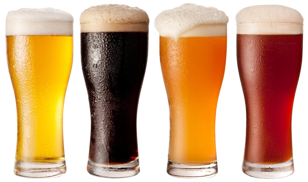 A display of four glasses of lager with froth spilling over the top. They range in color from deep brown, red brown, amber, and gold.