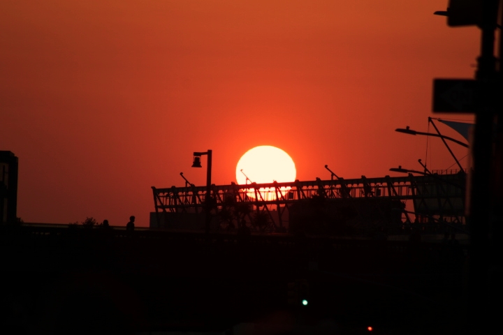 Manhattanhenge: a Celestial Phenomenon. As the sun descends its light becomes redder. The sun is silhouetted against a metal structure.