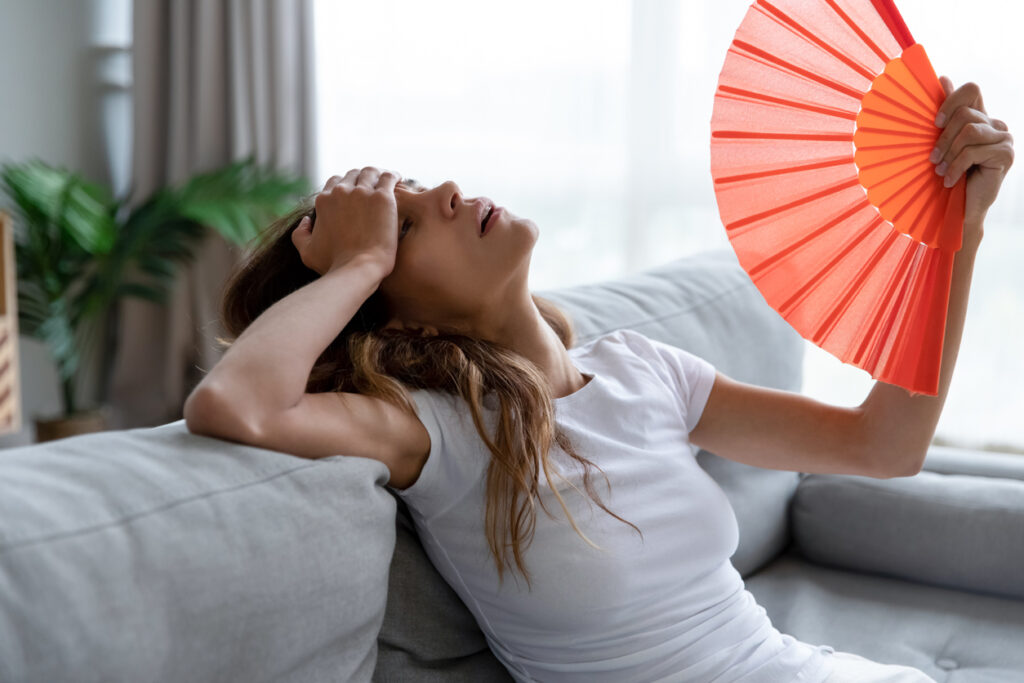 A young woman desperately fans herself to find relief from the heat.