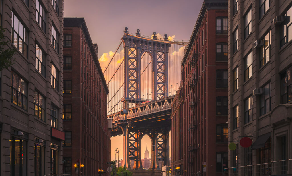 A photo showcasing the distinctive, industrial architecture that's been preserved in DUMBO or Down Under the Manhattan Bridge Overpass. The Manhattan Bridge is seen between the buildings in the distance.