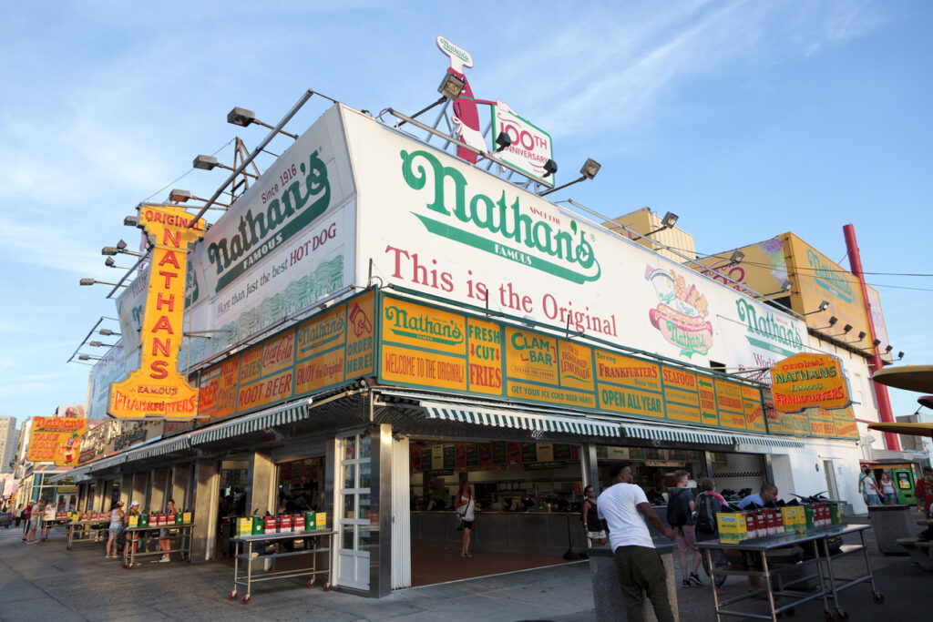 The original Nathan's on Surf Avenue in Coney Island, New York with its bold yellow, white, and green themed signs.