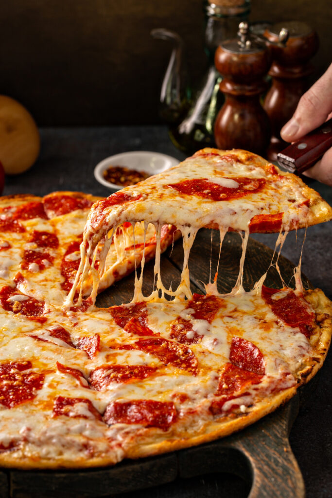 A Brooklyn-style pizza might feature pepperoni and cheese such as in this image of a slice of pepperoni pizza being lifted as cheese drips off the sides.