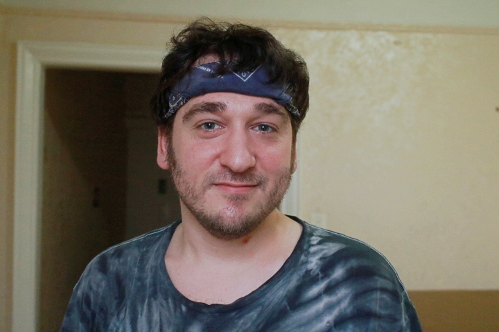 One of many faces of Brooklyn, Shaun Andrews. A man in his early 30s wearing a grey bandana headband and grey tie-dye t-shirt. 