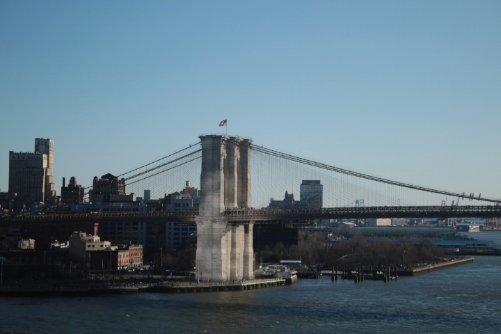 The Brooklyn Bridge illuminated by a building's reflection in the afternoon of Spring 2023.