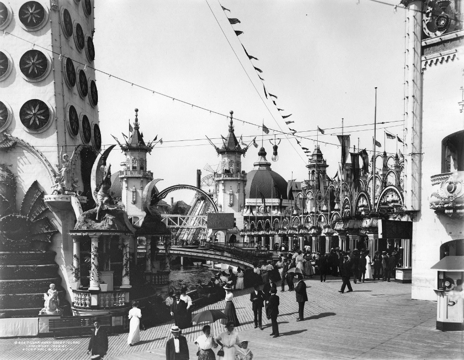 People walking through Luna Park during day with many fantastical looking buildings and statues.