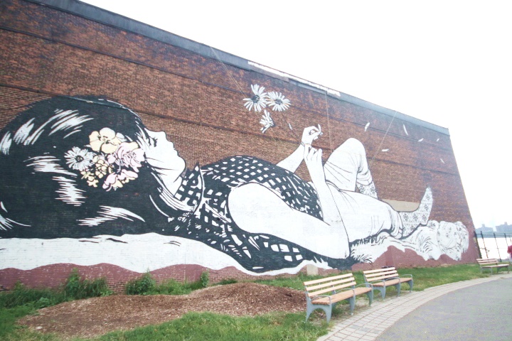 A giant wall mural of a girl picking flower petals in North Brooklyn.